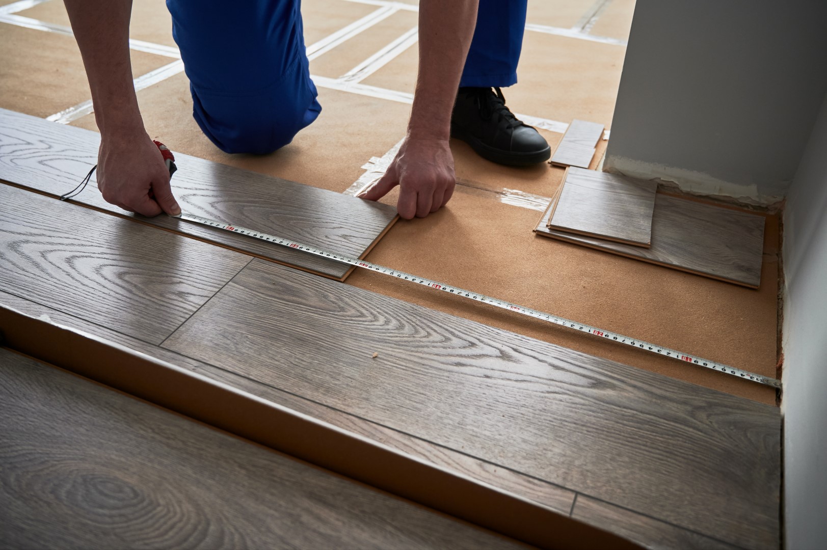 Close up of man construction worker checking distance from wall to laminate board. Male builder using tape measure while installing laminate flooring in apartment under renovation.